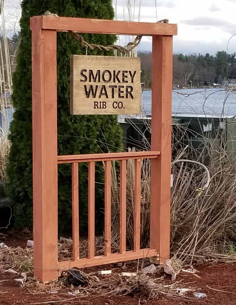 Carved wooden Smokey Water Rib Co sign by the lake.